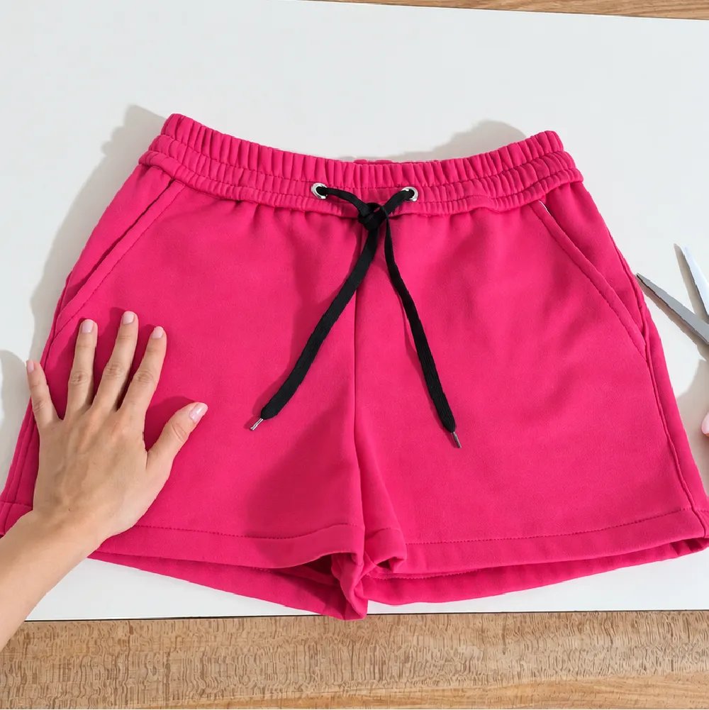 Mano sobre short deportivo fucsia con cordón, parte del diseño de patrones de costura PDF de Meiling Mendoza.